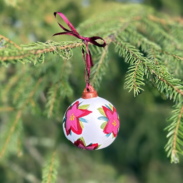 Bilde av håndmalt julekule hengende i et juletre. Julekulen er vakkert dekorert med blomsten julestjerne