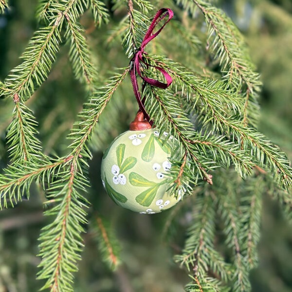 Bilde av håndmalt julekule hengende i et tre. Julekulen er lys grønn misteltein.