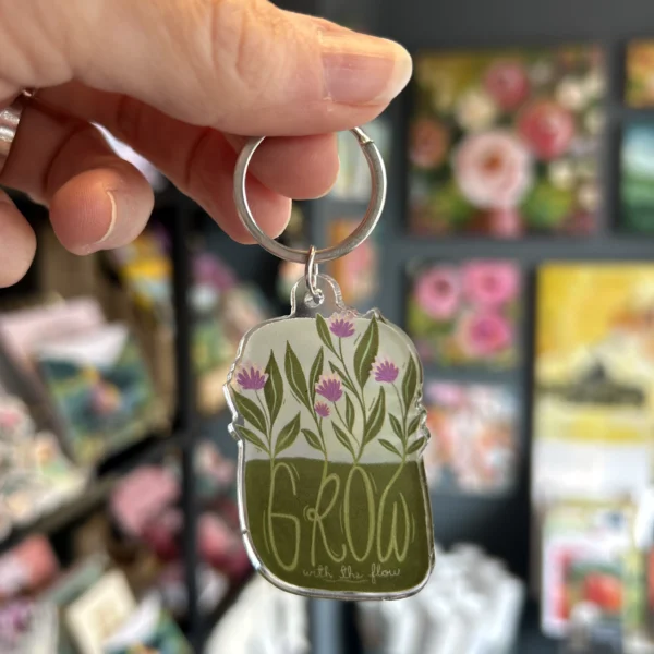Hånd som holder Nøkkelring med blomster og teksten Grow with the flow